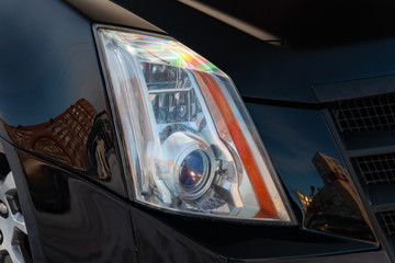 Front headlamp view of black used car stands in the auto showroom sale after washing and polish with orange turn light and bi-xenon lens. Auto service industry. © Aleksandr Kondratov