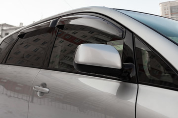 Close-up of the side left mirror with turn signal repeater and window of the car body silver SUV on the street parking after washing and detailing in auto service industry. Road safety while driving