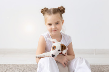 People, pets and animal concept - Little girl sitting on the floor over white background and holding puppy Jack Russell Terrier