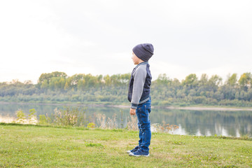 Children and childhood concept - young boy walking near the river