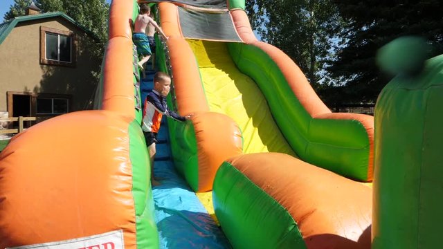 Slow motion shot of boy sliding down inflatable water slide at party