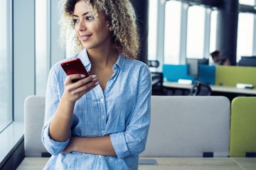 Smiling businesswoman using smartphone in office. Wearing in blue shirt