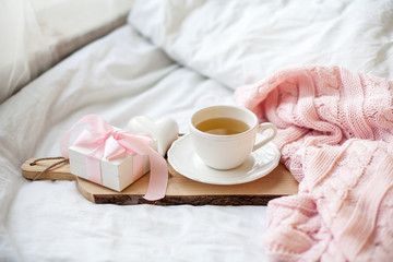 Obraz na płótnie Canvas White mug with tea, gift box with ribbon on the bed. Breakfast in bed. Cozy. Pink plaid. Cotton.