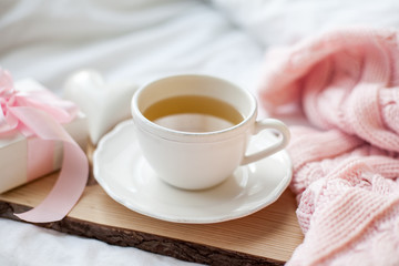 White mug with tea, gift box with ribbon on the bed. Breakfast in bed. Cozy. Pink plaid. Cotton.