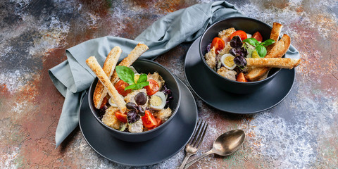 Food banner of Caesar salad with chicken, quail egg, cherry tomatoes, croutons and basil in dark blue bowls on a rusty background.