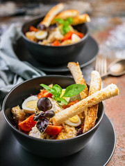 Vertical shot of two servings of Caesar salad with chicken, quail egg, cherry tomatoes, croutons and basil in dark blue bowls on a rusty background.