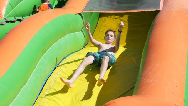 Slow motion shot of children sliding down inflatable water slide