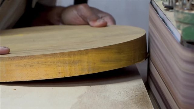 Close up of hands using a belt sander to smooth edges of round piece of wood