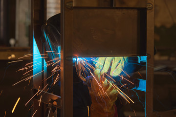 Welder welds metal parts, lots of smoke and sparks, harmfulness, worker