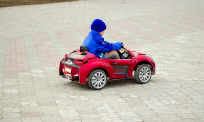 Fototapeta na wymiar The child riding a red electric car on the street. Baby rider.