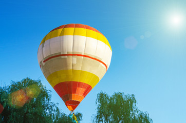 Colorful hot air balloon is flying in the blue sky above the trees