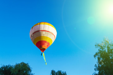 Colorful hot air balloon is flying in the blue sky above the trees