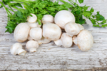 Uncooked button mushrooms with parsley on an old wooden surface