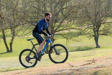 Fototapeta na wymiar Cyclist in shorts and jersey on a modern carbon hardtail bike with an air suspension fork rides off-road on green hills near the forest
