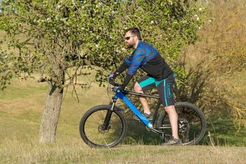 Fototapeta premium Cyclist in shorts and jersey on a modern carbon hardtail bike with an air suspension fork rides off-road on green hills near the forest