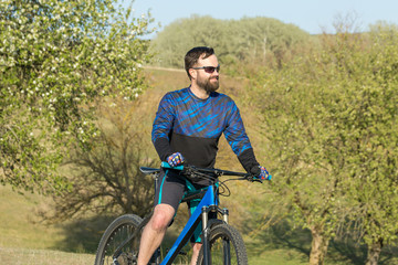 Naklejka premium Cyclist in shorts and jersey on a modern carbon hardtail bike with an air suspension fork rides off-road on green hills near the forest