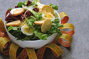 Healthy salad and measuring tape. The concept of losing weight on proper nutrition.