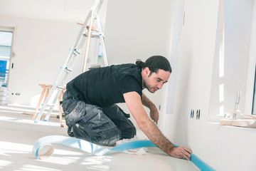 Workers in a flat work on a floor. glue edge insulation strip. balance the floor.