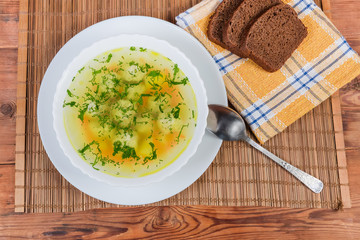 Top view of chicken meatballs soup in dish, spoon, bread