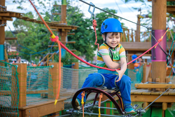 Obraz na płótnie Canvas Little cute boy enjoying activity in a climbing adventure park on a summer sunny day. toddler climbing in a rope playground structure.