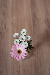 Blumenstrauss aus einer rosa pinken Gerbera und weissen Blumen in Glasvase auf Holzboden unten mittig platziert von oben fotografiert im Hochformat