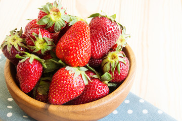 Strawberries in a bowl on a light wood background with place for text. Berry summer background.