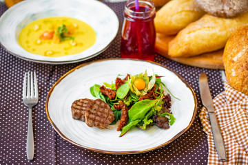  beautiful grilled steak, with green salad, sun-dried tomatoes and physalis on a white plate.  dinner.  dinner table.