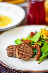  beautiful grilled steak, with green salad, sun-dried tomatoes and physalis on a white plate.  dinner.  dinner table.
