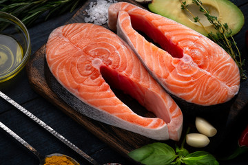 Raw fresh salmon steak with herbs, avocado, basil, lemon and garlic - ingredients for cooking on black wood background. Healthy food concept