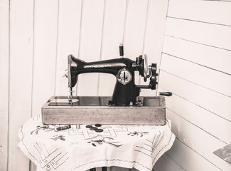 Side view of old cool grandmother`s manual sewing machine hand tool with crank on white wooden board background on table. Vintage arts and crafts concepts, sepia color tones.