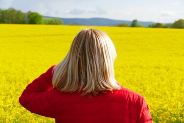 Frau mit blonden Haaren vor einem Rapsfeld