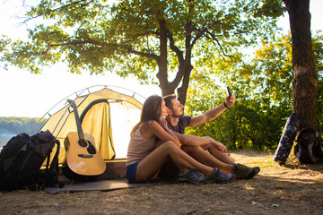 A man and a woman on a camping trip take a selfie near the tent.