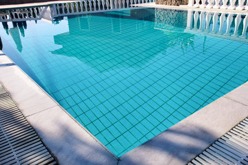 Swimming pool design modern architecture of luxury holiday villa. Relax near exotic swimming pool with handrail, deck chairs, sun loungers and parasols waiting for tourists in tropical resort hotel.