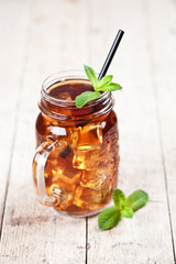 Traditional iced tea with lemon, mint leaves and ice cubes in glass jar on rustic wooden table.