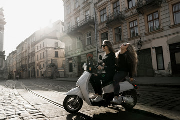 Young and beautiful girls in sunglasses riding a scooter. Portrait of pretty ladies riding a...
