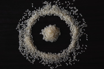 some amount of raw rice laying o the table ,creating a design.background is dark wooden table 