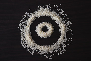 some amount of raw rice laying o the table ,creating a design.background is dark wooden table 
