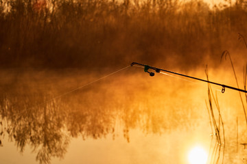 Fishing rod close-up at foggy sunrise on the lake , Sunrise over the lake reflected on the water surface