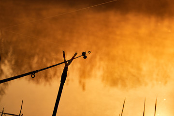 Fishing rod close-up at foggy sunrise on the lake , Sunrise over the lake reflected on the water surface