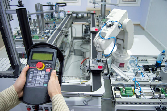 Man is holding teach panel (tablet) to control a robot arm which is integrated on smart factory production line. industry 4.0 automation line which is equipped with sensors and robotic arm.
