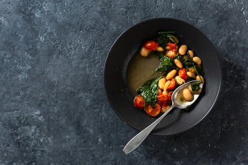 Dinner bowl of stewed white beans with vegetables on a dark background top view