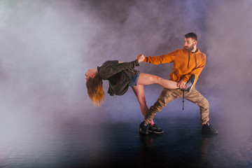 Fototapeta na wymiar Couple dancing modern dance and showing off their leg stretch moves.Black background while the couple is dressed in urban colorful clothes..