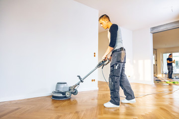 Fototapeta premium Einölen von Eichenparkett, Arbeiter mit poliermaschine und Werkzeug.