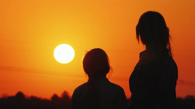 Mom and daughter look at the beautiful sunset over the city and the orange sky together