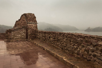 Ruins of the red brick walls of Czorsztyn Castle and itts reflecion on a rainy and foggy day. Ruins stand at the top of the hill nearby Dunajec River in he southernmost part of Poland. 