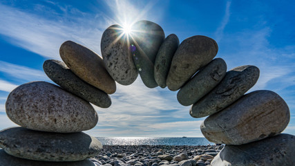 Stone arch on the shore of the Black Sea. Sun disk and blue sky on background, Sochi, Russia.