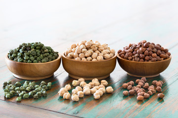 Colored chickpeas (red, green, white) in wooden bowls on rustic background.