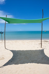 Beautiful beach view with a green tent on sunny summer day and sea and blue sky in the background. Concept of vacations, peace and relaxation. Ponta do Corumbau, Bahia, Brazil.
