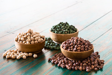 Colored chickpeas (red, green, white) in wooden bowls on rustic background.