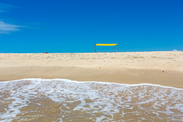 Fototapeta na wymiar Beautiful beach view from sea point of view and small yellow rustic tent on sunny summer day. Blue sky in the background. Concept of vacations, peace and relaxation. Ponta do Corumbau, Bahia, Brazil.